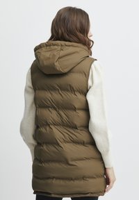 Olīvu zaļš pūkains bezmugurs, kas aprīkots ar kapuci, ar horizontālu šuvju rakstu, nedaudz garāku aizmuguri un gludu, spīdīgu tekstūru.