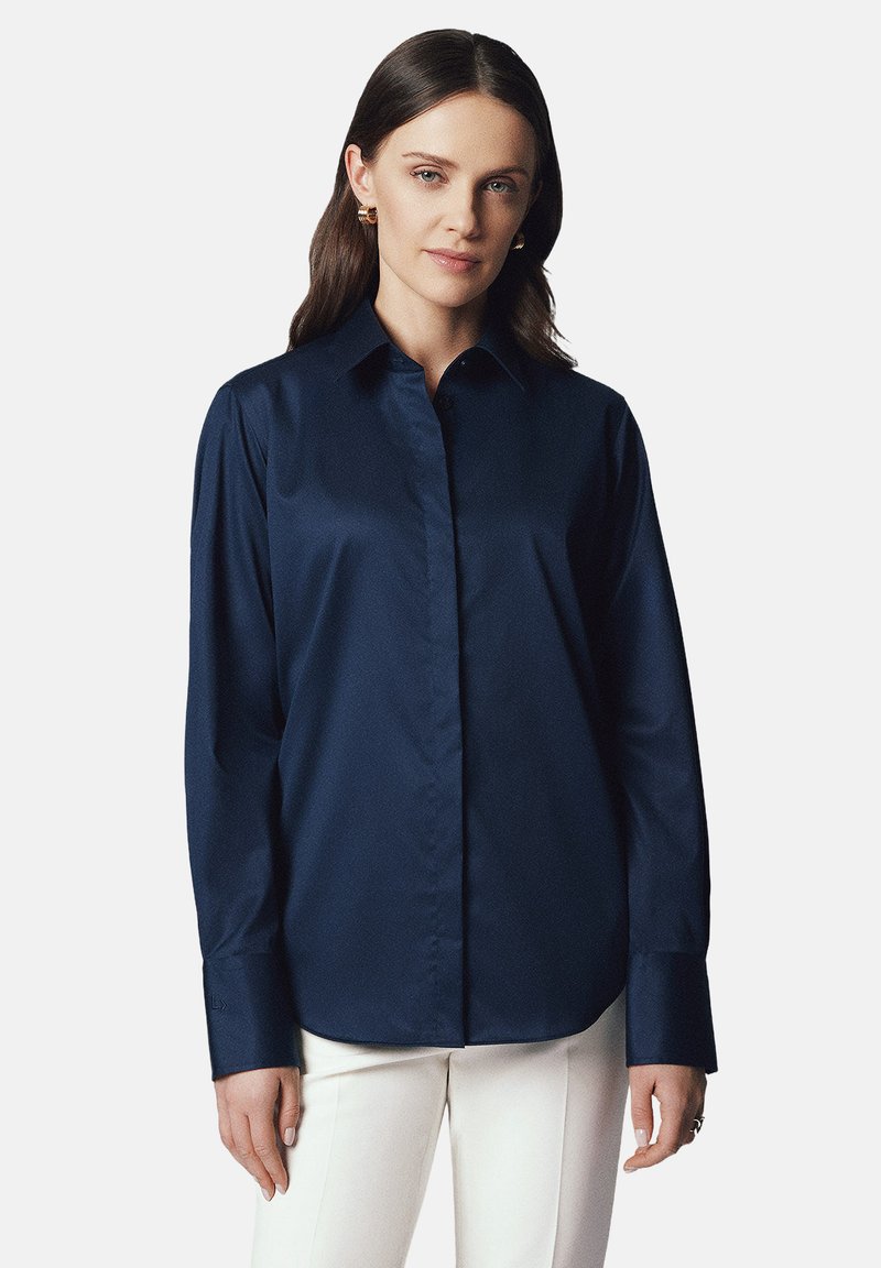 Granatowa koszula zapinana na guziki wykonana z gładkiego materiału; ma klasyczny kołnierzyk oraz długie rękawy z guzikiem; prosty krój.