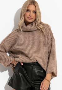 Jasnobrązowy sweter o żeberkowanej strukturze z golfem, w oversize'owym kroju i z opuszczonymi ramionami, w zestawie z czarnymi skórzanymi szortami.