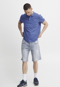 Blå piké med hvit trekantet mønster, kombinert med lyseblå denimshorts. Brukt med marineblå joggesko og hvite sokker.