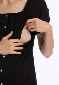 Zwarte stoffen top met knoopsluitingen, voorzien van een geraffineerd ontwerp en een beige kledingstuk dat eronder zichtbaar is, toegankelijk via de opening.