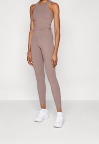 Conjunto de crop top y leggings deportivos en suave tela color topo, con diseño ajustado y textura sin costuras, combinado con zapatillas deportivas blancas.