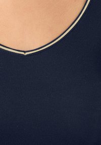 Marineblauw tanktop met een ronde hals en contrasterende gouden stiksels langs de rand; ribbelstructuur door de gehele stof.