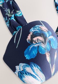 Marineblauer Stoff mit großem blau-weißem Blumenmuster, der eine detaillierte Nahaufnahme eines gepolsterten BH-Körbchens und eines gerafften Schulterbands zeigt.
