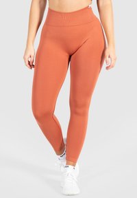 Hoogwaardige, naadloze leggings in een verbrand sinaasappelkleur, met een geribbelde tailleband en een slanke, rekbare pasvorm.