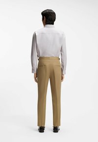 Vaaleanharmaa pitkähihainen paita, jossa on suora leikkaus ja napilliset kalvosimet, yhdistettynä beigeihin, takataskullisiin ja sileäpintaiseen räätälöityyn housuihin.