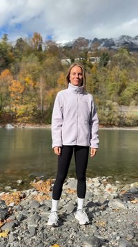 Šviesiai violetinė, užsegama flisinė striukė su aukštu apykakliu, dvi priekinės kišenės; derinama su juodomis tamprėmis ir baltais kojinėmis. Modelis stovi prie upės.