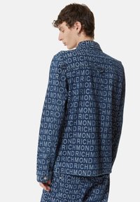 Giacca in denim con un motivo testuale "RICHMOND" su tutto il capo in azzurro chiaro su uno sfondo blu scuro. Colletto classico e dettagli con bottoni.