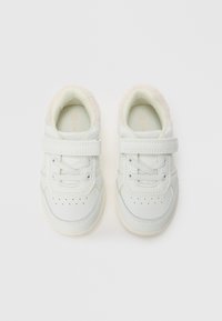 Une paire de baskets blanches pour tout-petits avec des bandes Velcro et des lacets, présentant des intérieurs rembourrés doux sur un fond blanc uni.