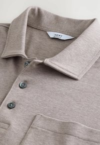 Beige polo-shirt med ribbet krave, brystlomme, tre mørke knapper og "NEXT" label. Lavet af blød, strikket stof.