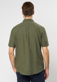 Camicia a maniche corte con bottoni di colore verde oliva, realizzata in tessuto testurizzato, con orlo dritto e yoke sulle spalle.