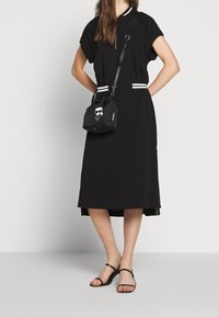 Black knee-length dress with short sleeves, white athletic stripes at the neck and waist. Paired with a small black bag featuring a skull graphic.