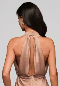 Vue arrière d'une robe sans manches, couleur brun clair, avec un col haut, un tissu drapé et une ouverture en V profonde. Présente deux boutons au niveau du col.