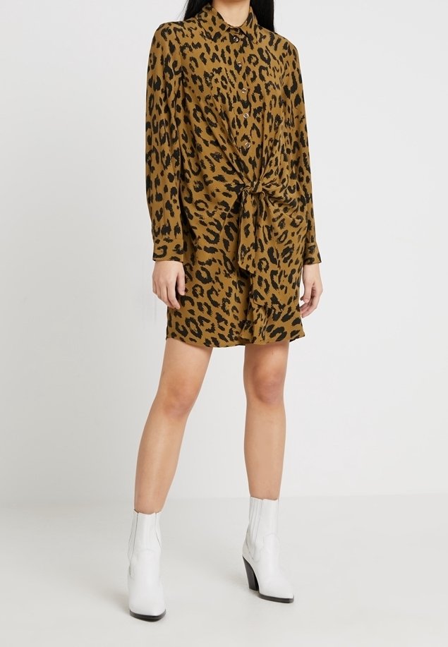 Abito camicia in stampa leopardata nei toni del marrone, con dettaglio alla vita legata, maniche lunghe e chiusura a bottoni. Indossato con stivaletti bianchi.
