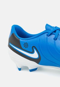 Sininen synteettinen jalkapallokenkä, jossa musta yksityiskohta ja valkoinen Nike-merkki. Kenkässä on teksturoitu pinta ja nauhakiinnitys varman istuvuuden takaamiseksi.