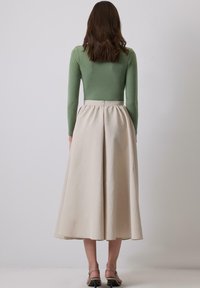 Long-sleeve, olive green top paired with a beige, A-line, knee-length skirt. The skirt features a gathered waist and smooth texture.