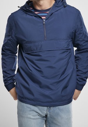 Navy blue pullover jacket with a half-zip, hood, front pocket, and elastic cuffs, made from smooth, water-resistant material.