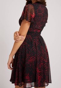 Robe noire avec motif de feuilles de palmier rouges, manches courtes transparentes, taille cintrée et jupe évasée, mettant en valeur une texture fluide et un tissu léger.