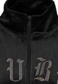 Chaqueta de terciopelo negro con cremallera, que presenta diseños decorativos de strass en la parte delantera, cuello alto y tejido texturizado.