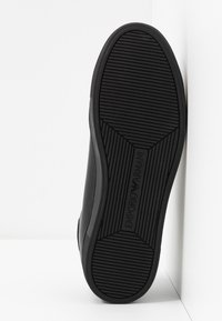Semelle de chaussure en caoutchouc noir avec des rainures horizontales et diagonales, comportant le logo embossé « Emporio Armani ». Bords lisses ; design plat.