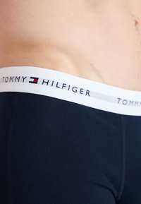 Sötétkék pamut boxer alsónadrág fehér rugalmas derékkal, amelyen a "TOMMY HILFIGER" logó és egy jellegzetes logó díszítés található. Sima tapintás.