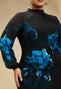 Rochie neagră cu design floral albastru, mâneci lungi din material transparent și accente cu paiete. Prezintă un gât înalt și o siluetă ajustată.