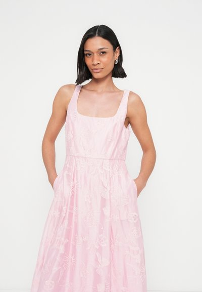 Robe rose sans manches avec un décolleté carré, présentant une broderie florale et des poches sur les côtés ; silhouette fluide et tissu léger.