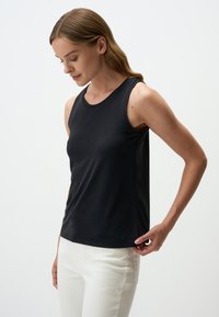 Canotta nera senza maniche realizzata in tessuto liscio e leggero, con scollatura rotonda e design aderente, abbinata a pantaloni bianchi.