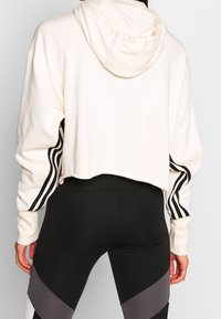 Felpa corta color crema con un cappuccio e corde di serraggio, con strisce nere sulle maniche, abbinata a leggings alti in vita neri e grigi.