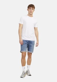 White cotton t-shirt paired with rolled hem denim shorts in light blue. Worn with gray sneakers and white crew socks, standing on a light backdrop.