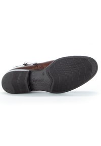 Brązowe skórzane buty z teksturowaną czarną gumową podeszwą. Szczegółowe przeszycia wzdłuż cholewy oraz małe logo na podeszwie. Płaski design.