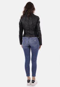 Giubotto di pelle nera con design attillato, dettagli delle cuciture in evidenza e maniche lunghe. Abbinato a jeans skinny blu e sneakers bianche.