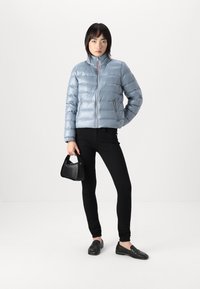 Lys blå pufferjakke med horisontalt quiltet design, høy krage og frontglidelås. Kombinert med svarte skinnyjeans og en liten svart håndveske.
