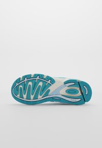 Suola di una scarpa da corsa bianca e turchese che mostra un motivo dettagliato del battistrada e elementi di ammortizzazione con marchio, su uno sfondo semplice.