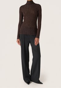 Brun ribbade turtlenecktröja med långa ärmar, tillsammans med högmidjade svarta vida byxor och spetsiga svarta klackar. Slät tygstruktur.