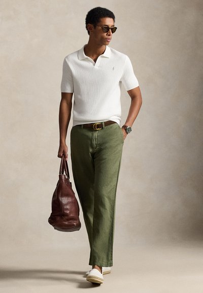 White ribbed polo shirt, olive green pants, brown leather bag, and white espadrilles. Accessories include dark sunglasses and a watch.
