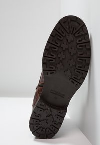 Botte en cuir marron avec une semelle en caoutchouc texturée dotée d'un motif de traction, un détail de fermeture éclair et une marque en relief sur la semelle. Taille 42.