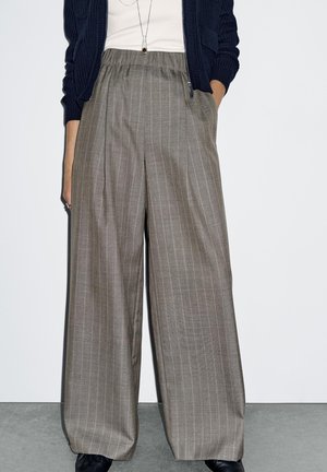 Gray, wide-leg trousers with vertical stripes, elastic waistband, front pockets, and a soft texture. Worn with a navy cardigan and white top.