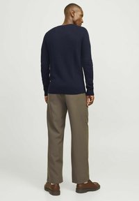 Maglione a coste blu navy con maniche lunghe, abbinato a pantaloni khaki larghi e scarpe in pelle marrone, che mostrano una silhouette rilassata.