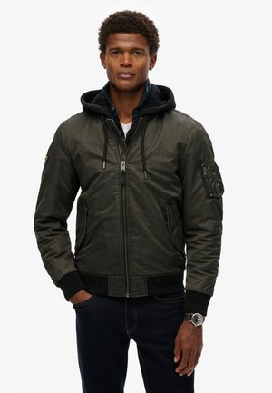 Green bomber jacket with a hood, zip closure, ribbed cuffs, side pockets, and left arm pocket detail. Smooth texture with a matte finish.