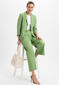 Grüne Blazer und passende weite Hose aus leichtem Stoff. Kombinieren Sie es mit einem weißen Oberteil, einer beigen Handtasche und hellbraunen Riemchenheels für einen stimmigen Look.