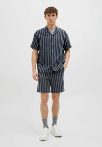 Kortærmet skjorte med knapper og matchende shorts i mørk marineblå med lodrette lyseblå striber; lavet af struktureret stof. Hvide sneakers.