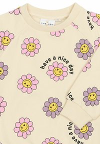 Beez õhkkleid pusa roosa ja lilla naeratavate karikakarde lilledega ning musta värviga trükitud fraasiga "tore päev" ees ja varrukal.