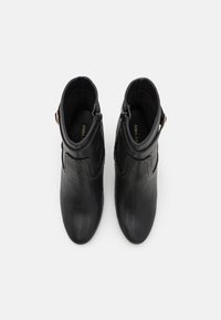 Černé kožené kotníkové boty s hladkým povrchem, špičatou špičkou a ozdobným prošíváním. Boční zip a doplňkové ozdobné kovové detaily.
