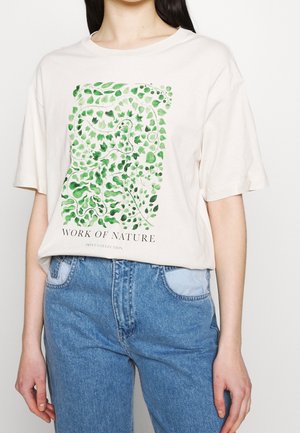 Weißes T-Shirt mit grünem Aquarell-Blattmuster und Text "WORK OF NATURE", getragen mit hoch taillierten blauen Jeans.
