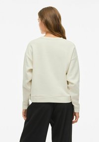 Felpa beige chiaro con una vestibilità comoda, scollatura rotonda e spalle scese. Presenta un orlo con spacchi laterali e un tessuto morbido e testurizzato.
