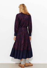 Robe à manches longues en violet foncé avec un motif floral, taille cintrée et une jupe fluide qui passe au bleu marine à l'ourlet.