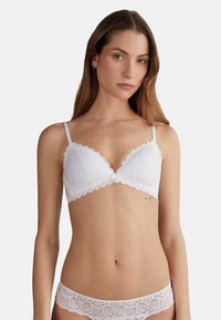 Witte kanten bralette met geschulpte randen en verstelbare bandjes. Bloemenpatroon en zachte stof. Bijpassende kanten onderbroek zichtbaar.