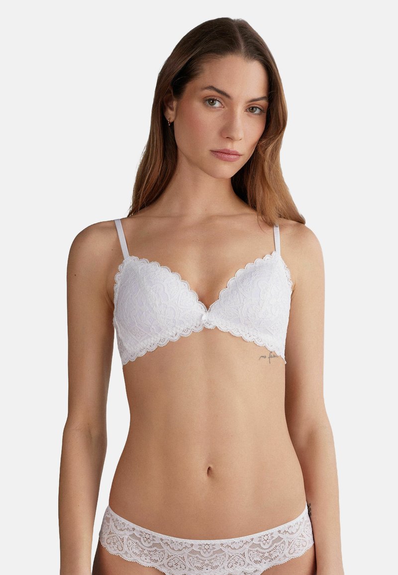 Witte kanten bralette met geschulpte randen en verstelbare bandjes. Bloemenpatroon en zachte stof. Bijpassende kanten onderbroek zichtbaar.