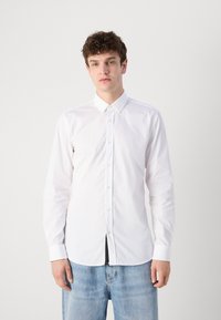Camisa blanca de manga larga con cuello puntiagudo, textura suave y cierre frontal de botones, combinada con jeans de mezclilla azul claro.